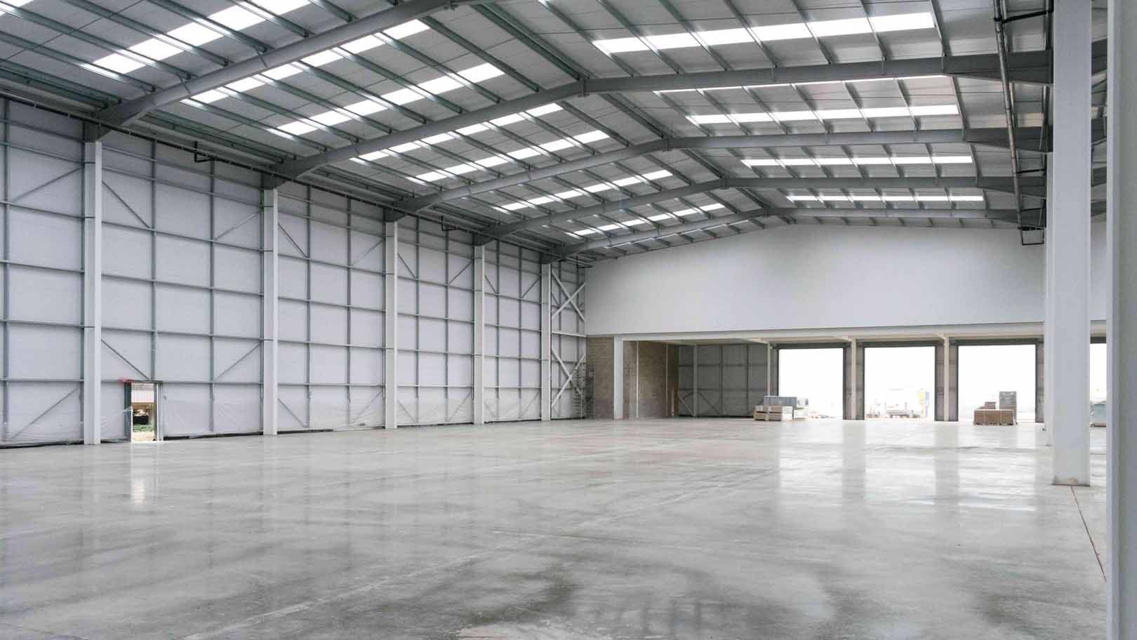 A large, empty warehouse with a steel roof structure and smooth concrete floor
